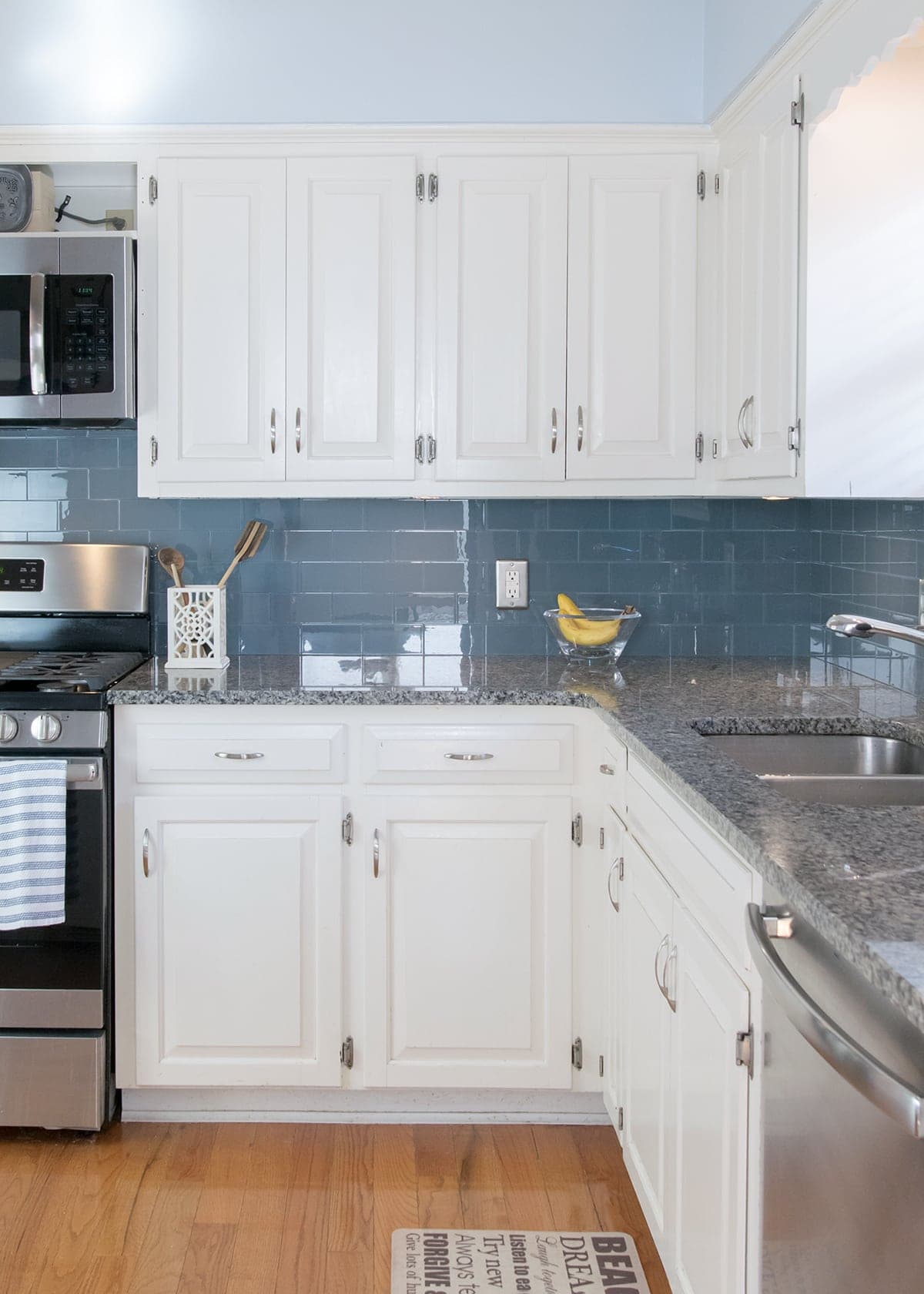 Peel and stick backsplash after installation in kitchen with white cabinets and grey countertops.