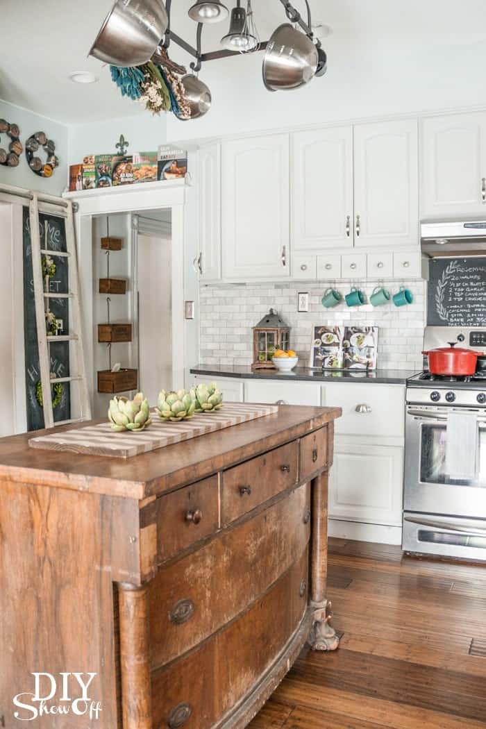 Eclectic Modern kitchen with white cabinets and backsplash, rustic wood island, and artful chalkboards.