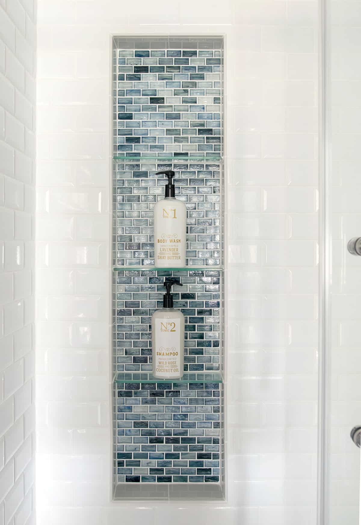 large shower niche with glass tiles and glass shelves. Blue glass shower inset with white subway tile surround