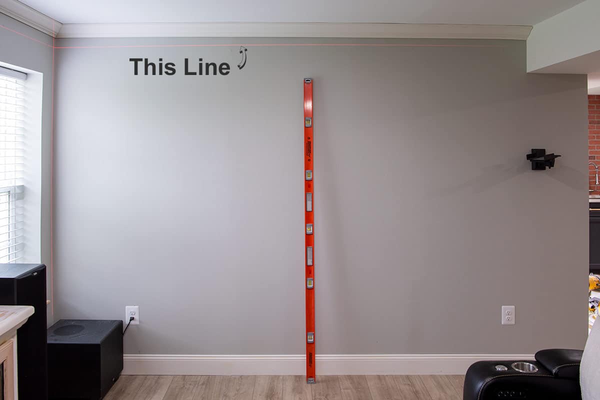 A blank wall with a long level leaning against it and a laser level line at the top to show that the wall is not level.