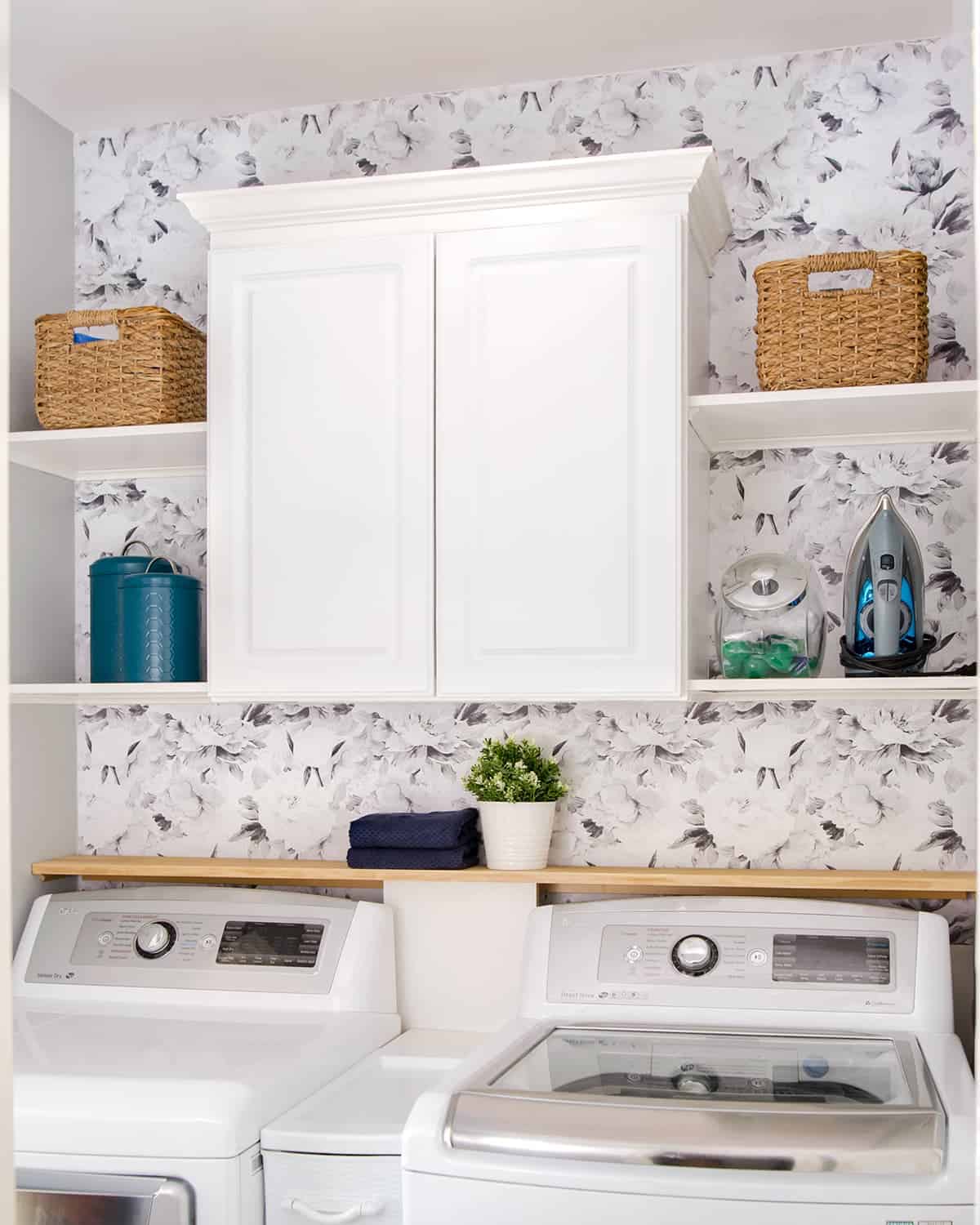 Small laundry room decorating idea with white cabinets, floral wallpaper, and teal accents.
