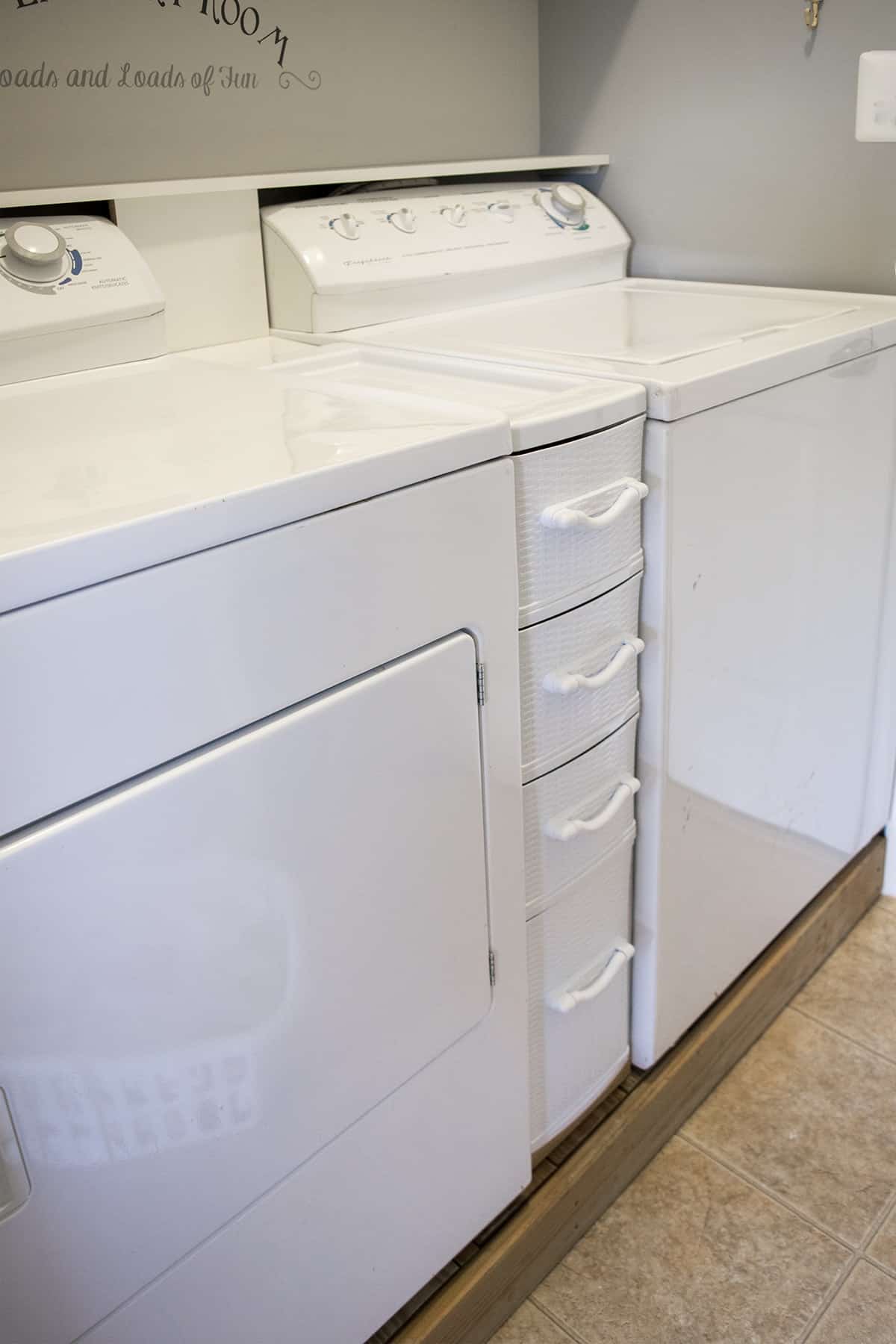 Washer and dryer on a platform with white storage console between them for easily organizing laundry supplies.