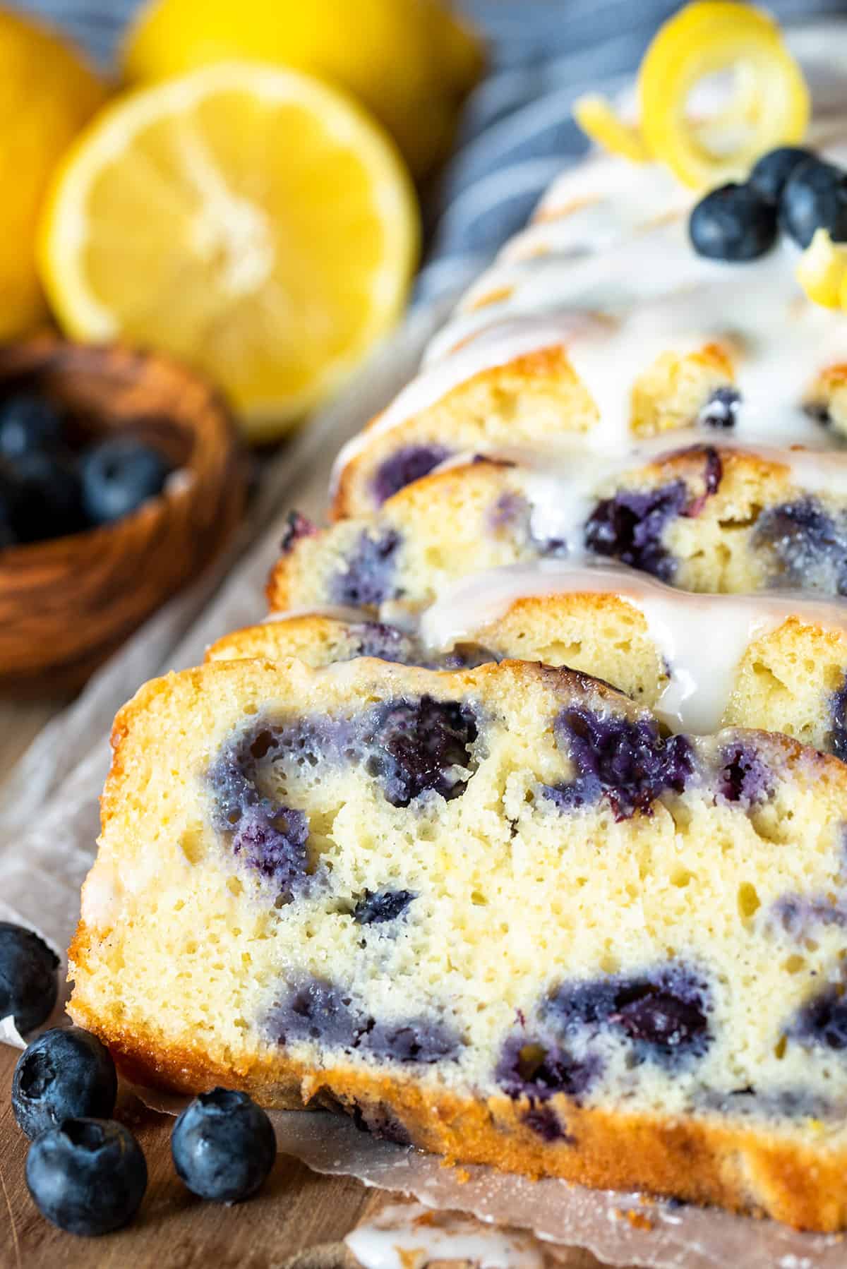 Sliced blueberry lemon bread with icing and lemons as garnish.