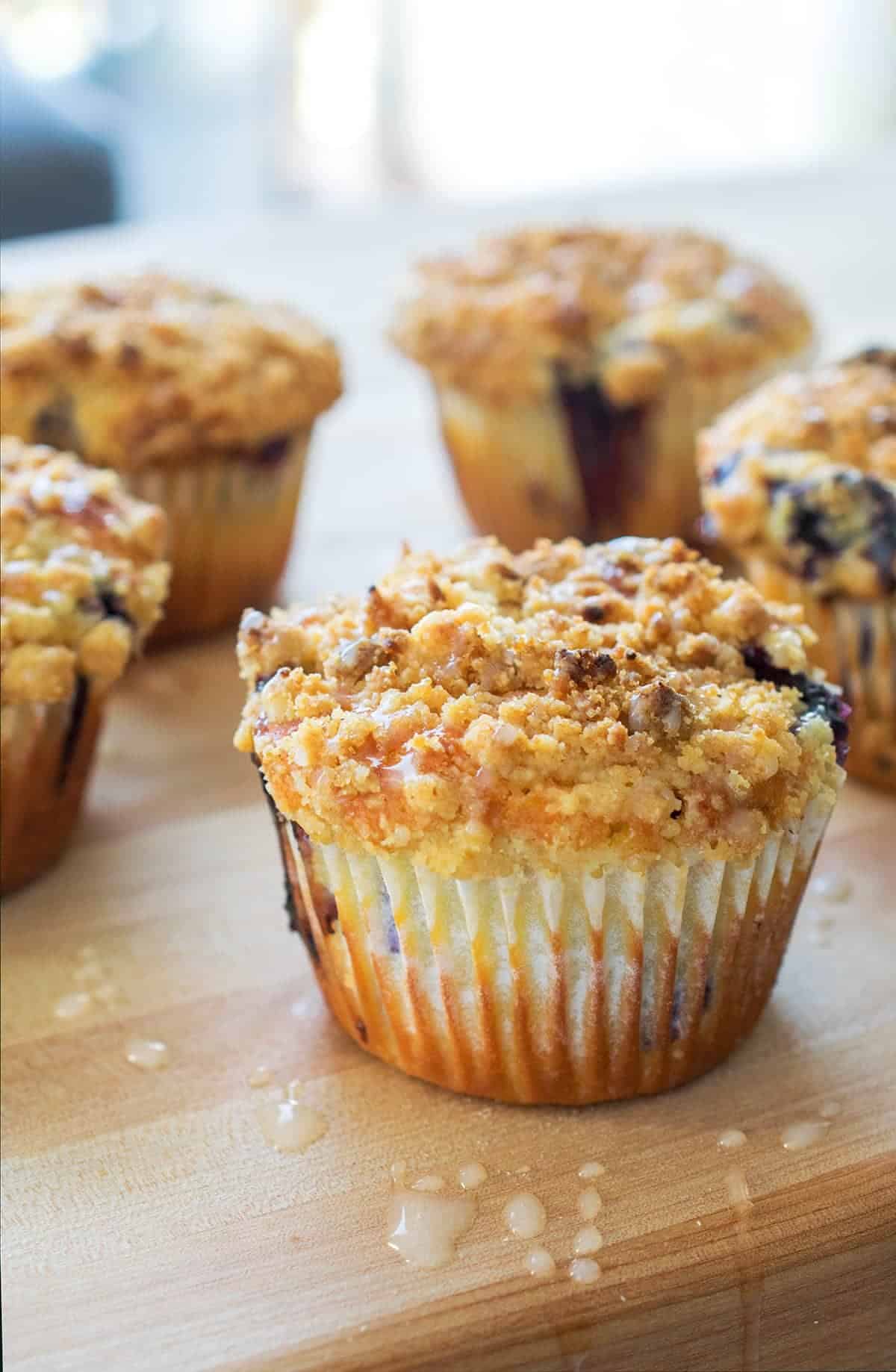 Lemon blueberry muffins with crumb topping on wood surface with sugar drips.