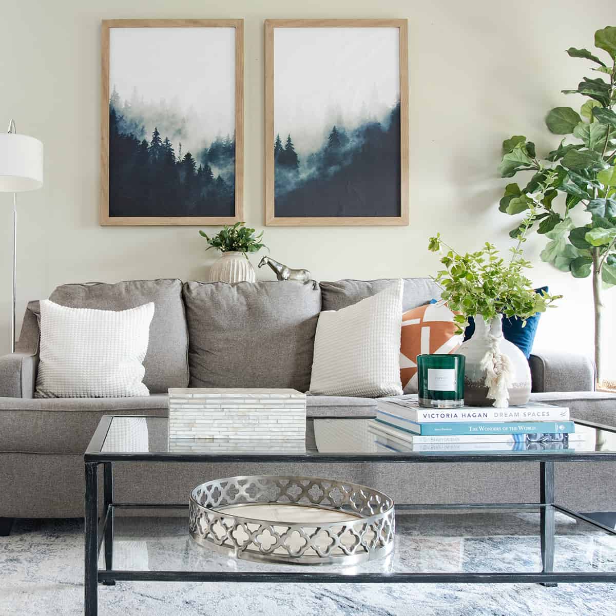 Light grey couch with colorful accents and glass coffee table filled with fresh greenery.