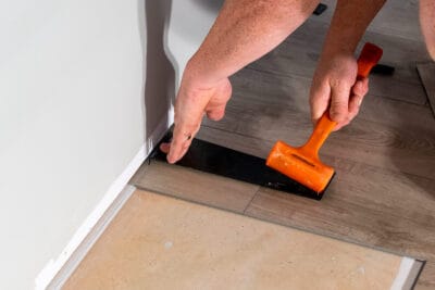 Man using a pull bar for vinyl flooring installation next to wall.