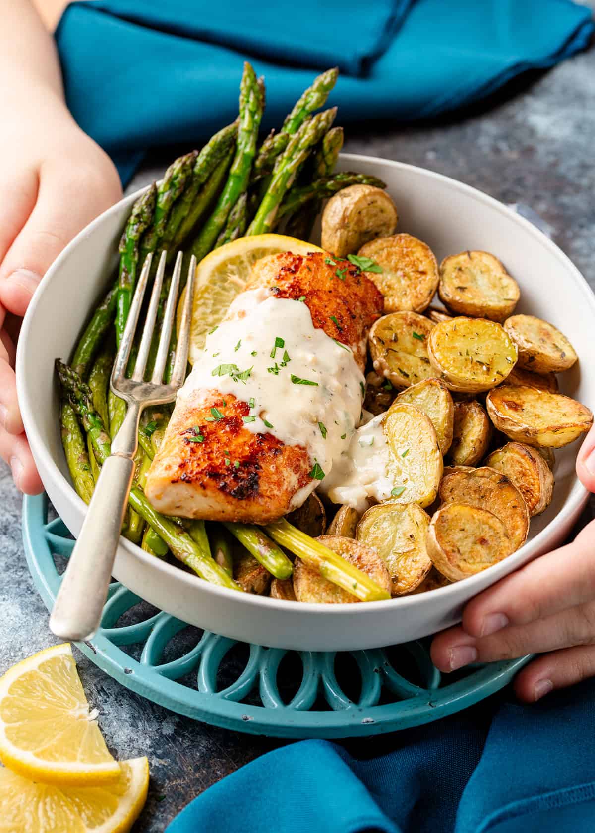 A boy holding a plated mahi with garlic cream sauce served with roasted asparagus and baby potatoes.