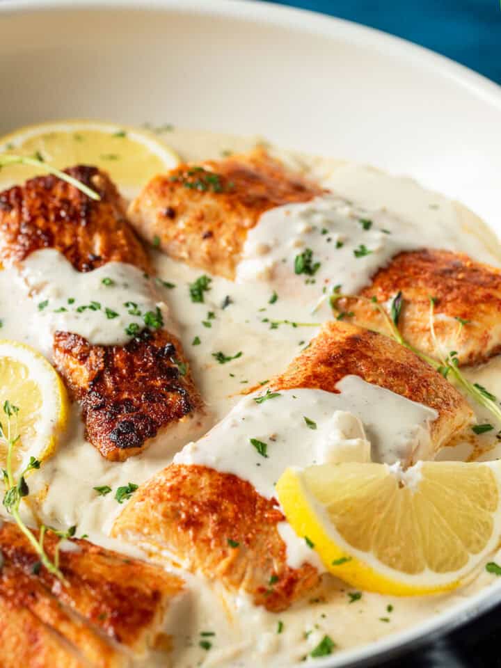 Filets of mahi-mahi in a skillet with garlic sauce, lemon slices, and fresh herbs.