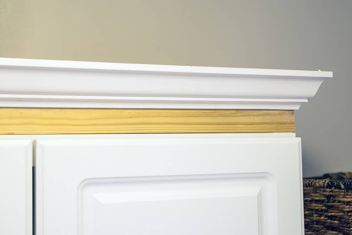 Corner of top of white cabinet with framing piece and trim attached.
