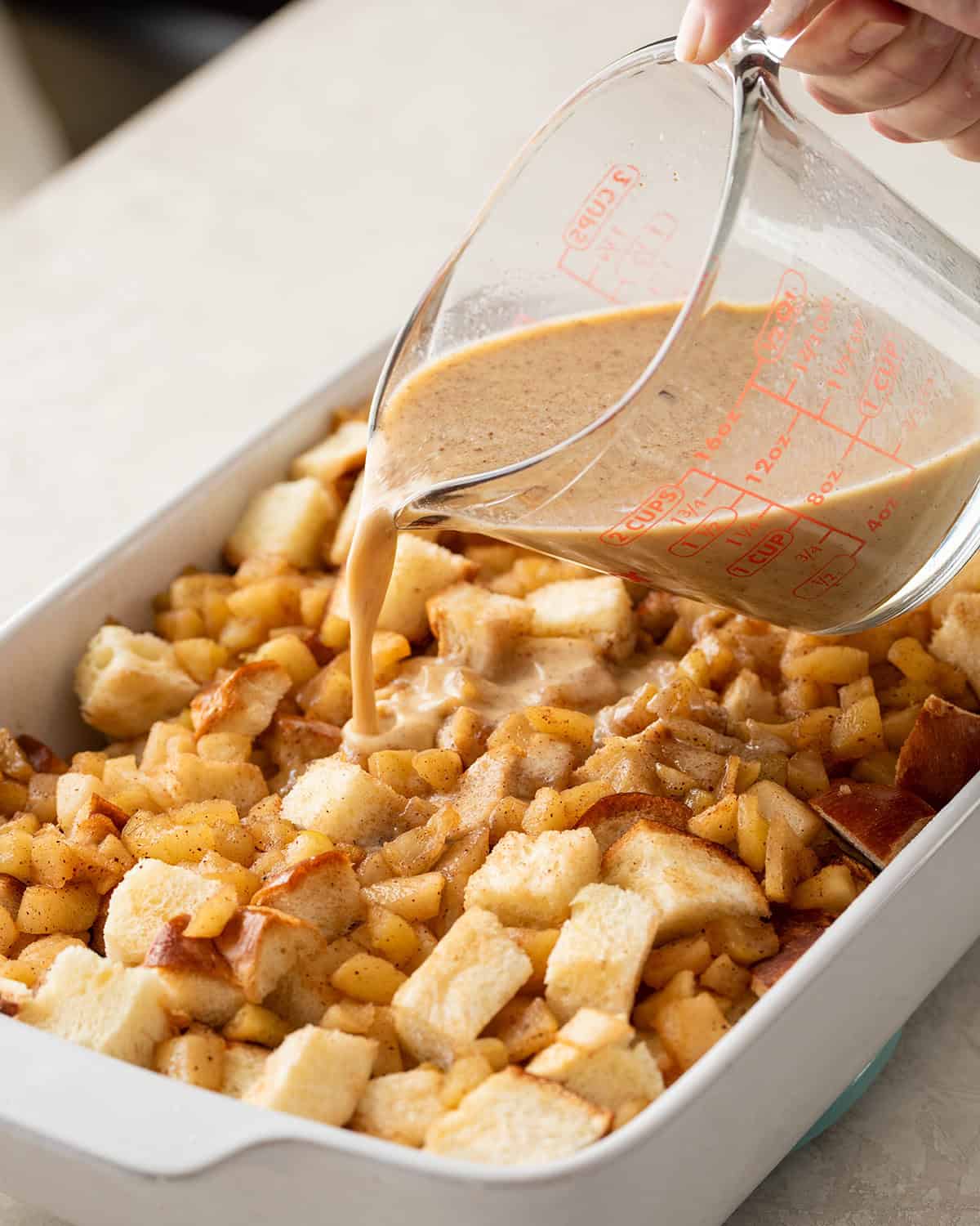 Woman pouring bread pudding sauce over bread before baking.