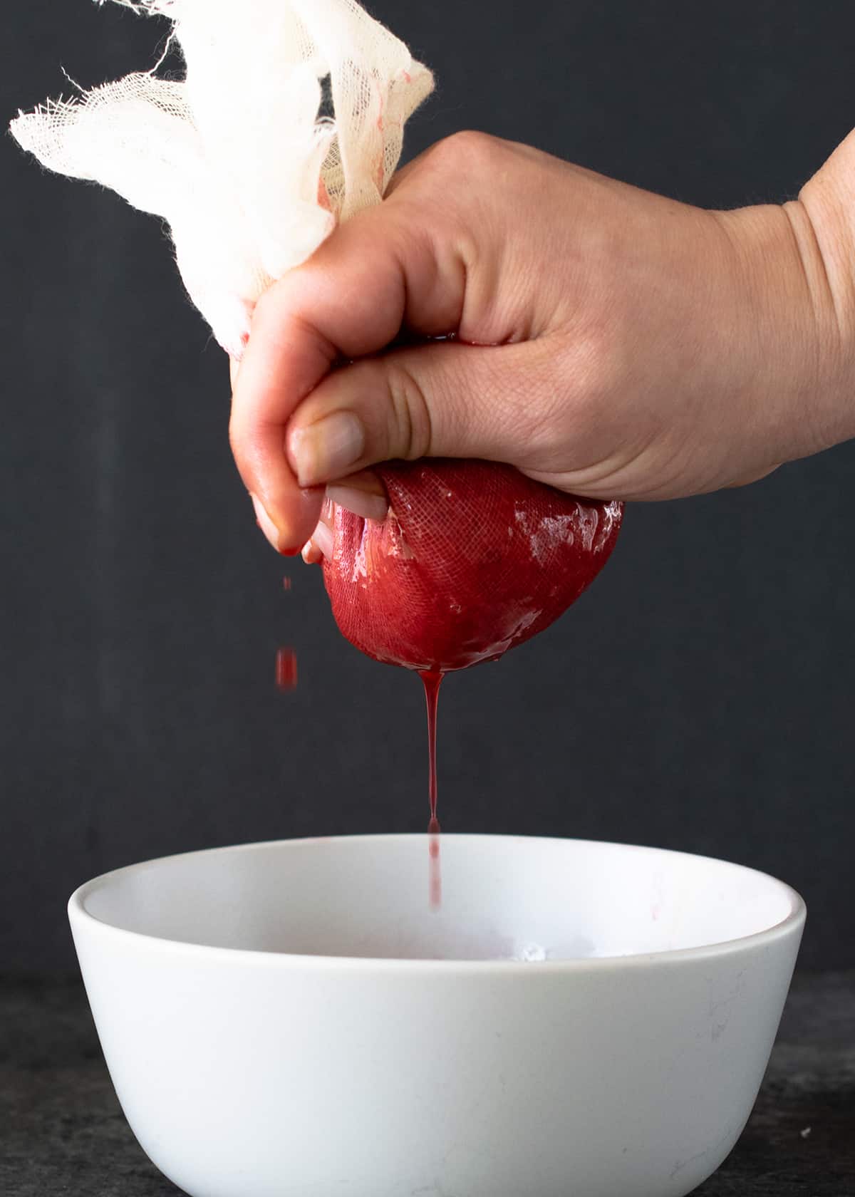 Strawberry puree being squeezed through cheesecloth in a bowl to make strawberry syrup.
