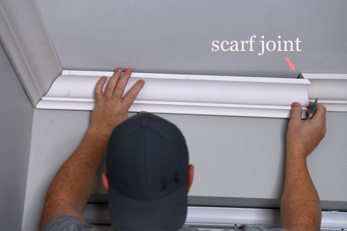 A man dry fitting coped molding and measuring the scarf joint.
