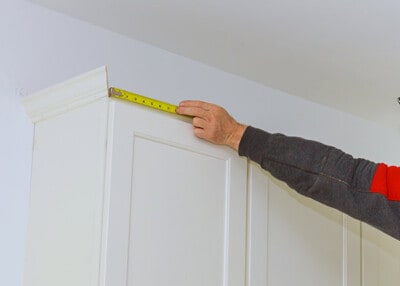 Measuring tape being held up to top of cabinets.