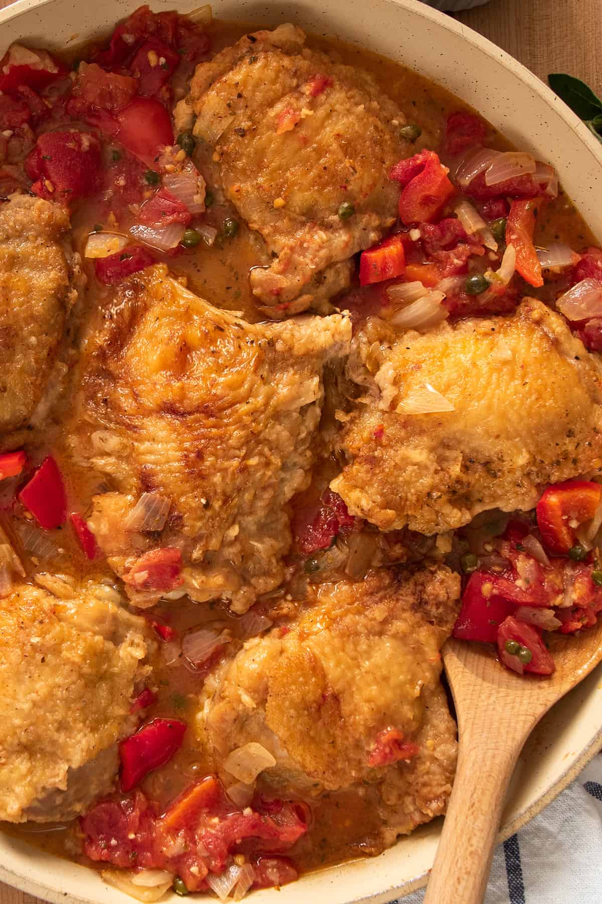 Top down look of chicken cacciatore in a pan with wooden spoon stirring.