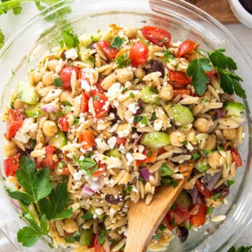 Overhead view of Mediterranean orzo mixture in a glass bowl with feta and parseley sprinkled over top.