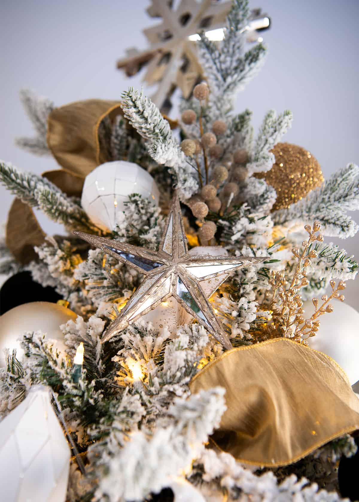 Looking upward at a snowflake Christmas tree topper with a mirrored gold ornament star in focus.