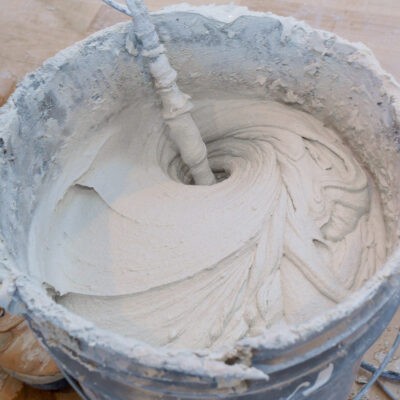 Mortar being mixed in a bucket with a paddle.