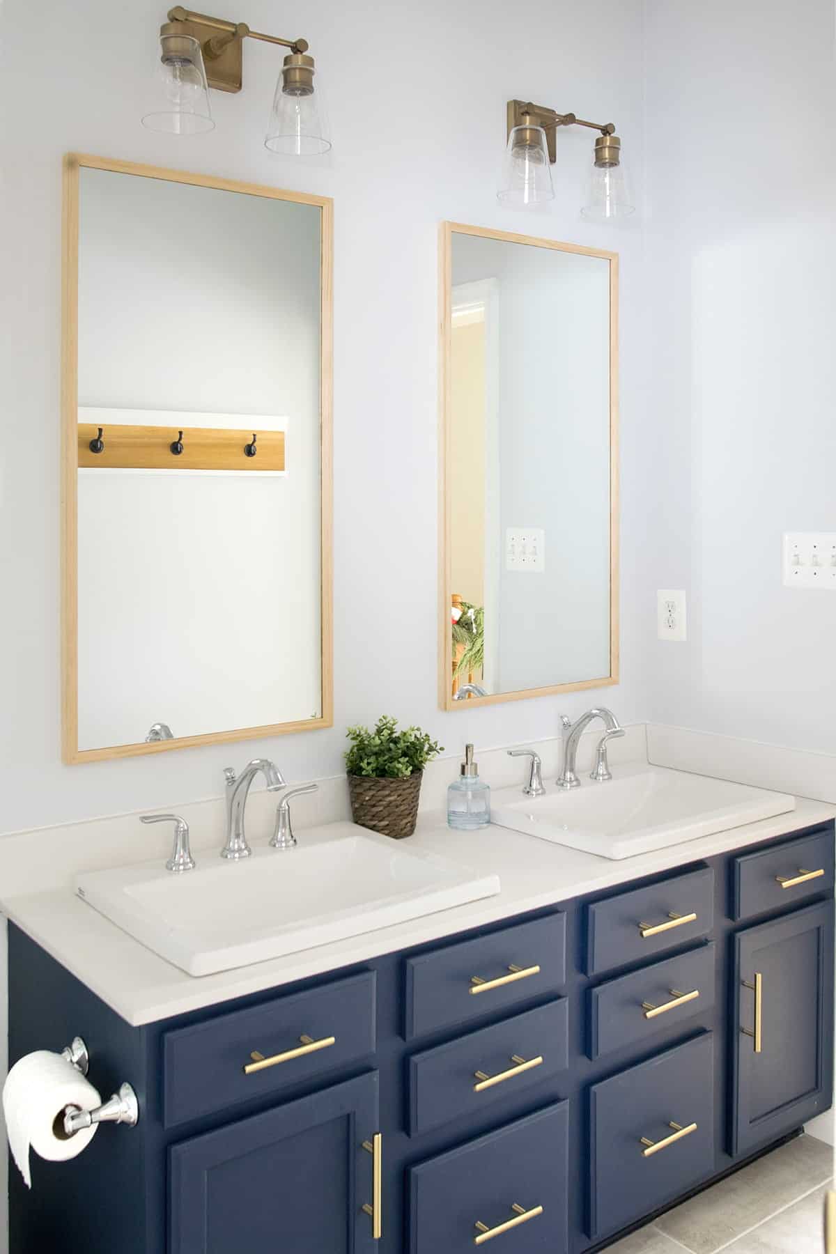 Bathroom vanity with two tall mirrors that have wood frames and lights over them.