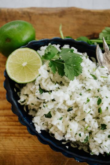 Closeup overhead of cilantro lime rice in a dish with a lime wedge garnish.
