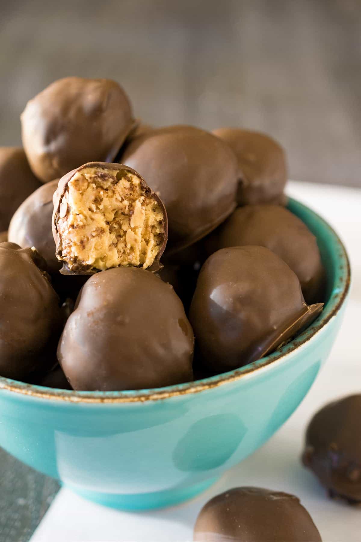 A bowl of peanut butter balls with one bite taken out to show inner texture.