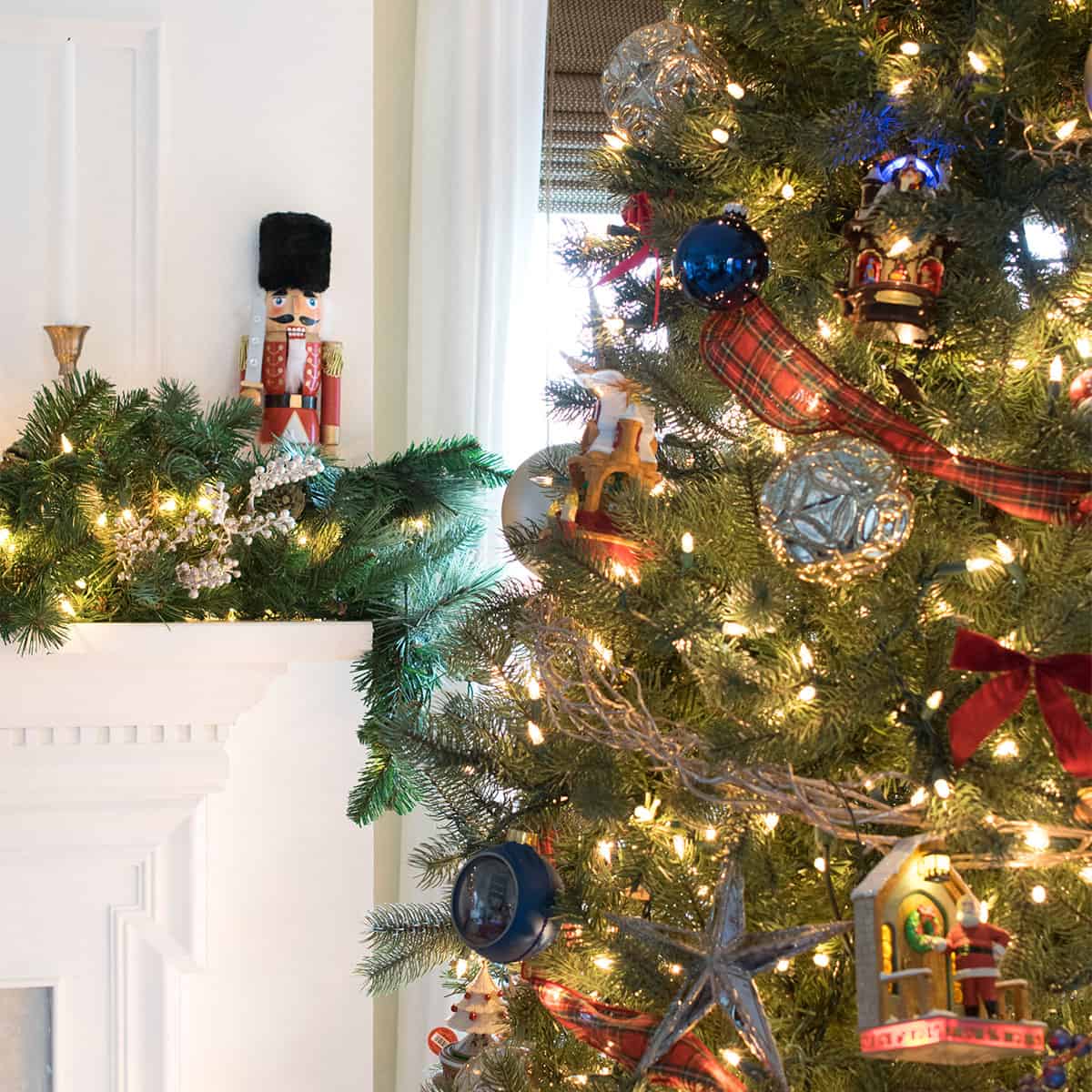 A nutcracker on a fireplace mantle next to a lighted Christmas tree with red and blue ornaments.