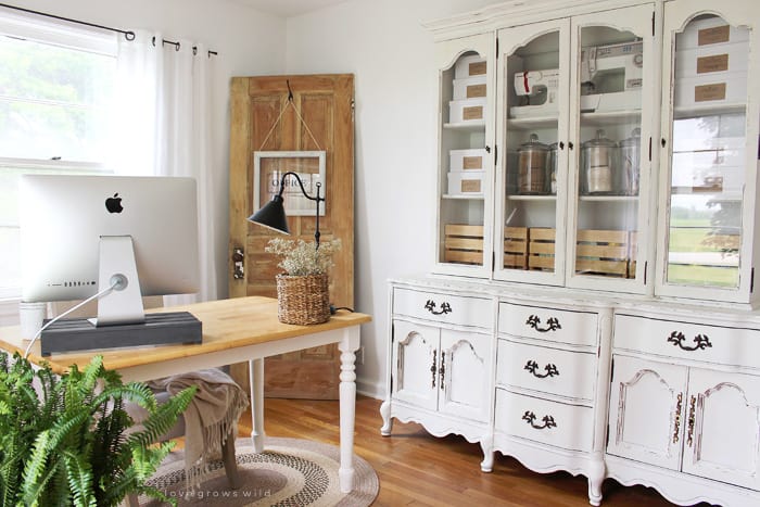White farmhouse dining room with large display hutch that has craft supplies in it and glass jars which is awesome for organizing your craft room in a useful way!