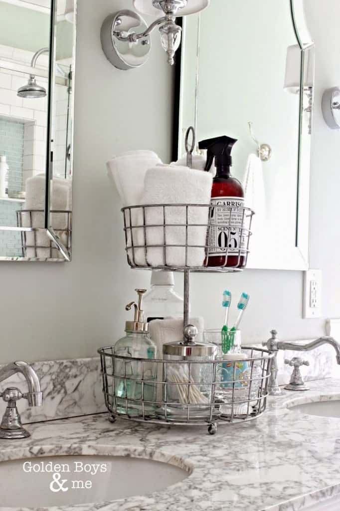 2-tiered wire metal basket tray on marble bathroom counter for storing small linens and toiletries.