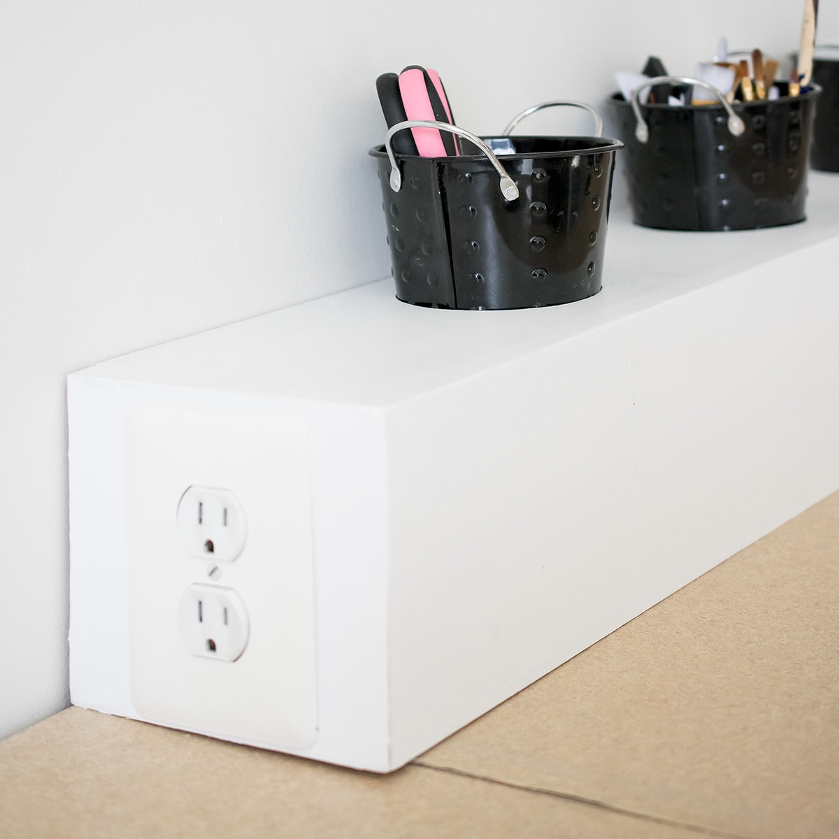 Office supply cups for crafting on a white wood box with outlets.