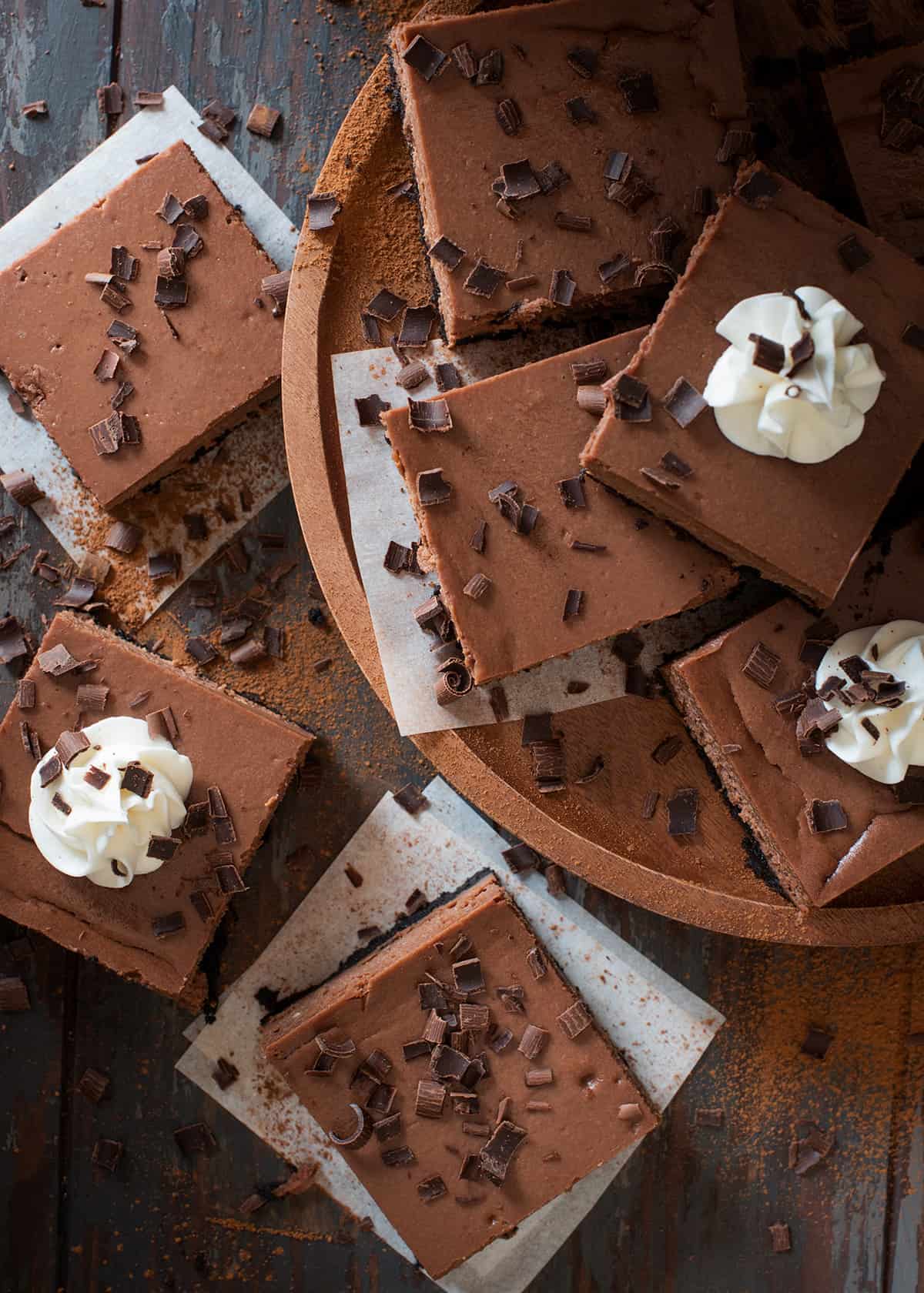 A tray of chocolate cheesecake bars with whip cream viewed from overhead.