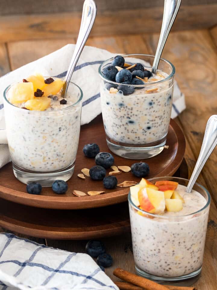 Three jars of almond milk overnight oats with various toppings on a wood background.