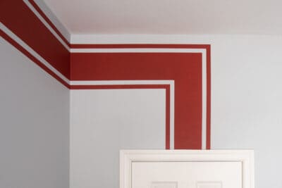 Single horizontal stripe in red racing stripe motif painted on a wall.