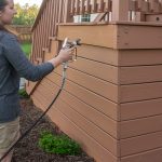 Woman staining a deck with a paint sprayer.