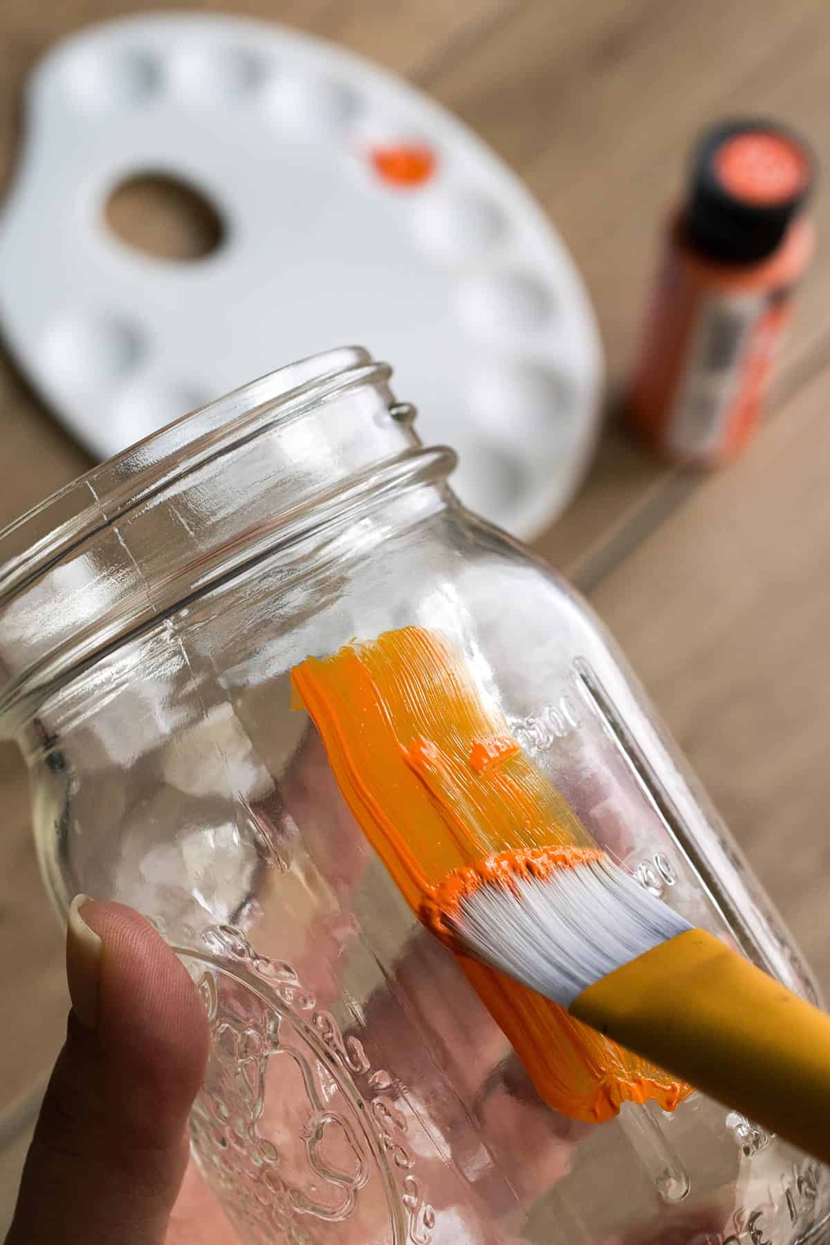 Painting glass mason jar orange for DIY basketball inspired mason jar project.