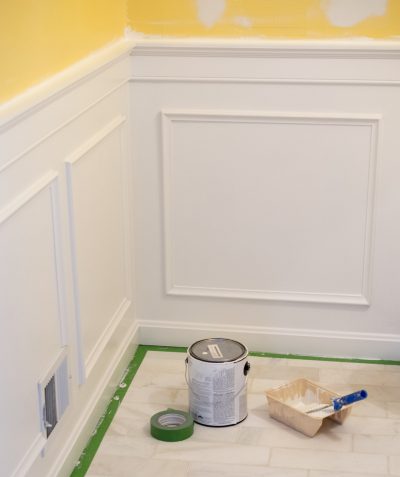 Painting wainscotting and chair molding with can of paint on the floor.