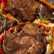 Pan seared pork chops in skillet with vegetables around.