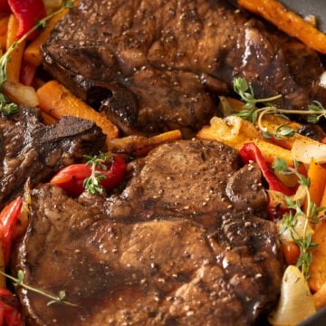 Pan seared pork chops in skillet with vegetables around.