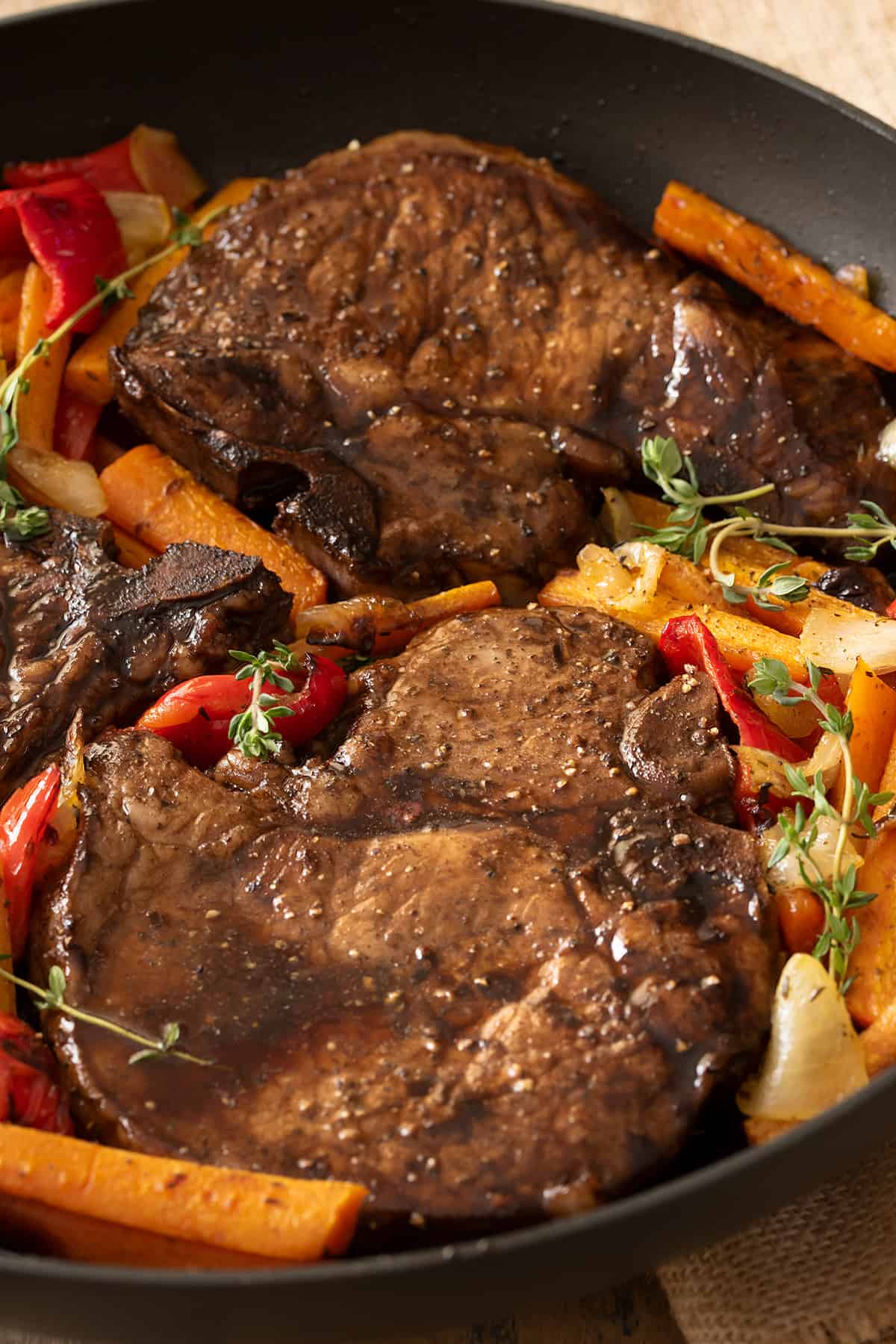 Pan seared pork chops in skillet with vegetables around.