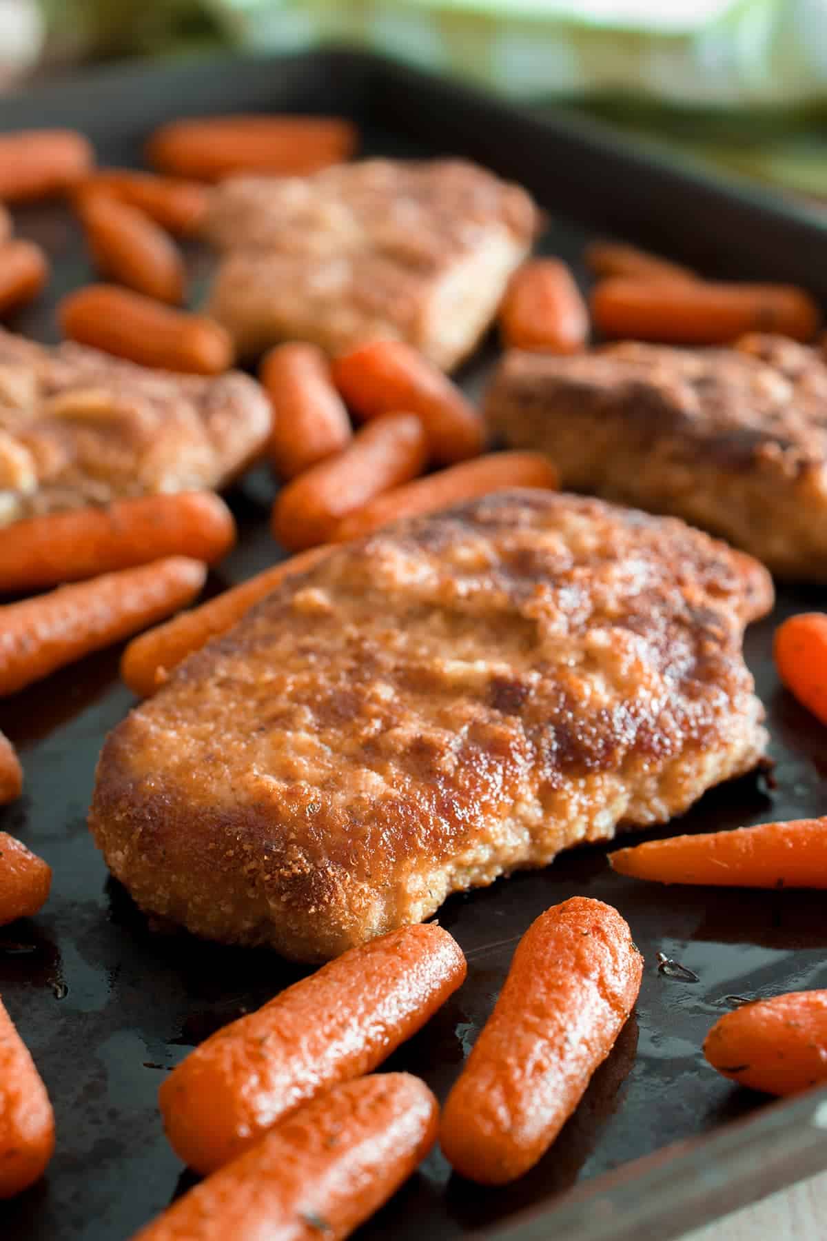 Oven baked breaded pork chops on a sheet pan with roasted baby carrots