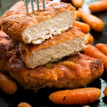 Breaded baked pork chops with baby carrots. Top pork chop sliced in half with fork piercing through it.