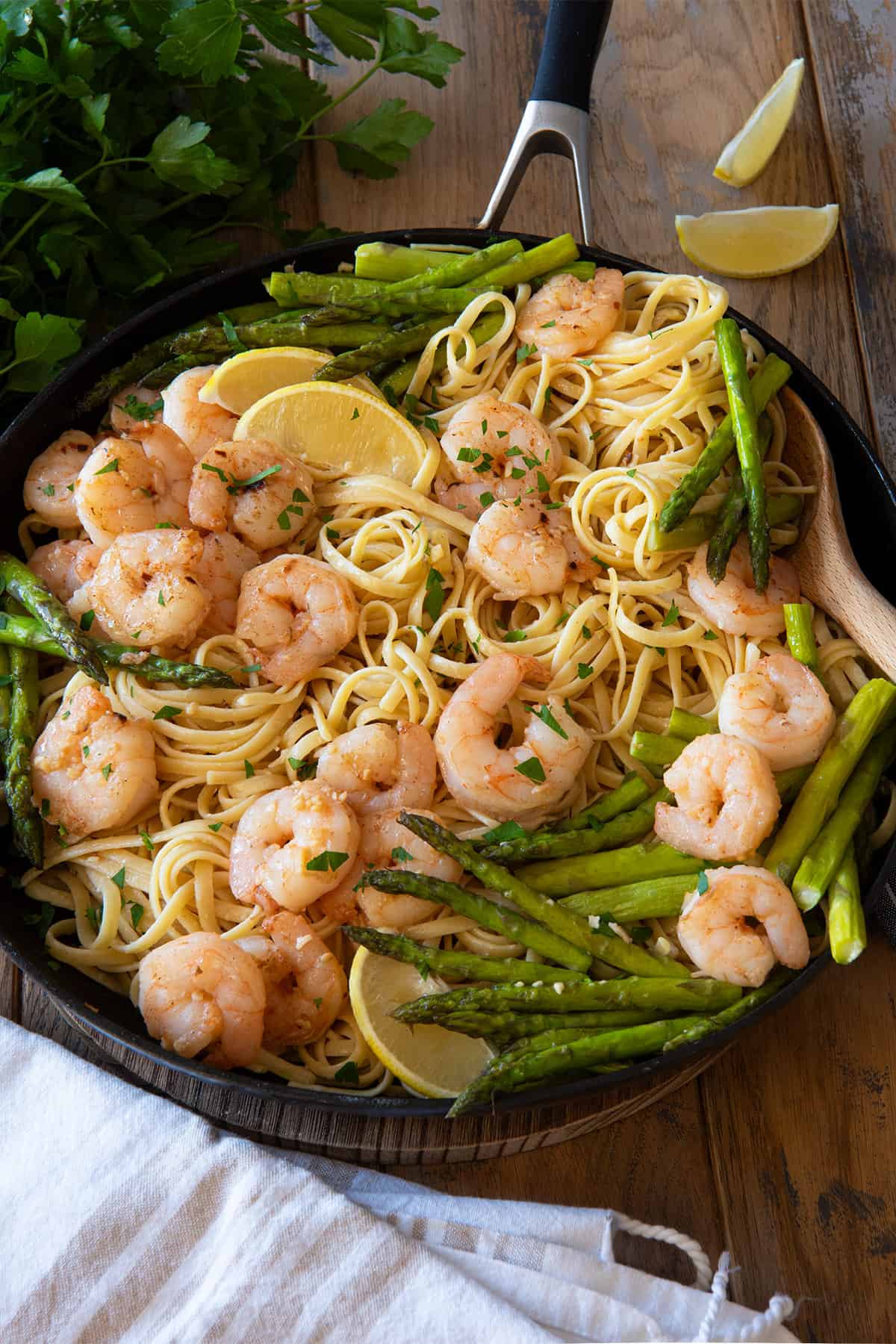 A skillet filled with shrimp asparagus linguine pasta with lemon slices as garnish.
