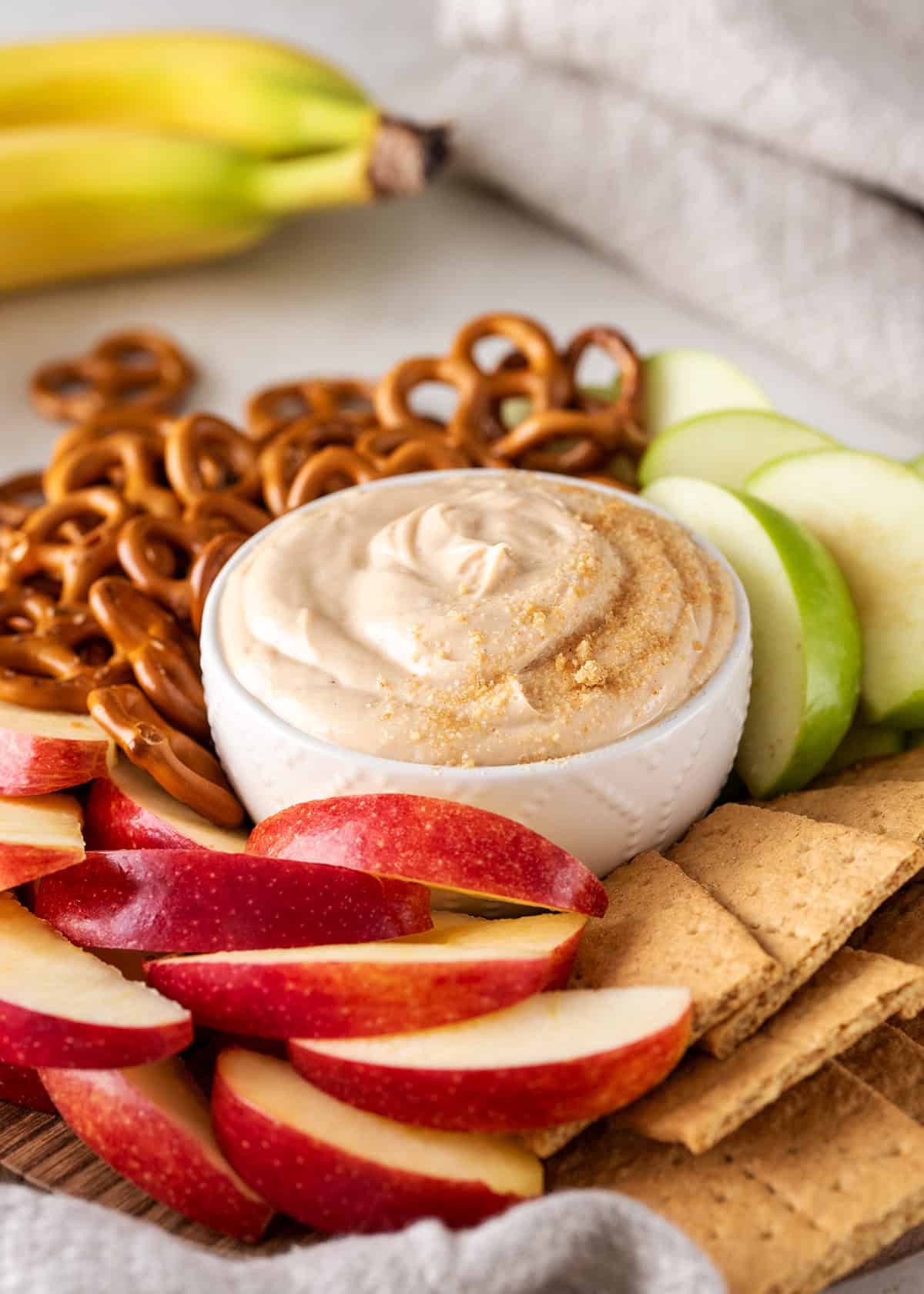 Closeup of peanut butter dip in a bowl with apple slices, graham crackers, and pretzels around.