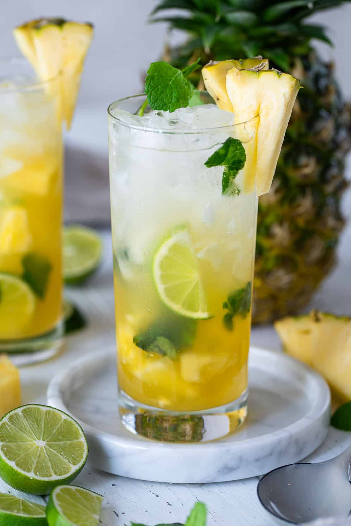 A pineapple mojito in a tall glass with lime slices and pineapple wedges as garnish.