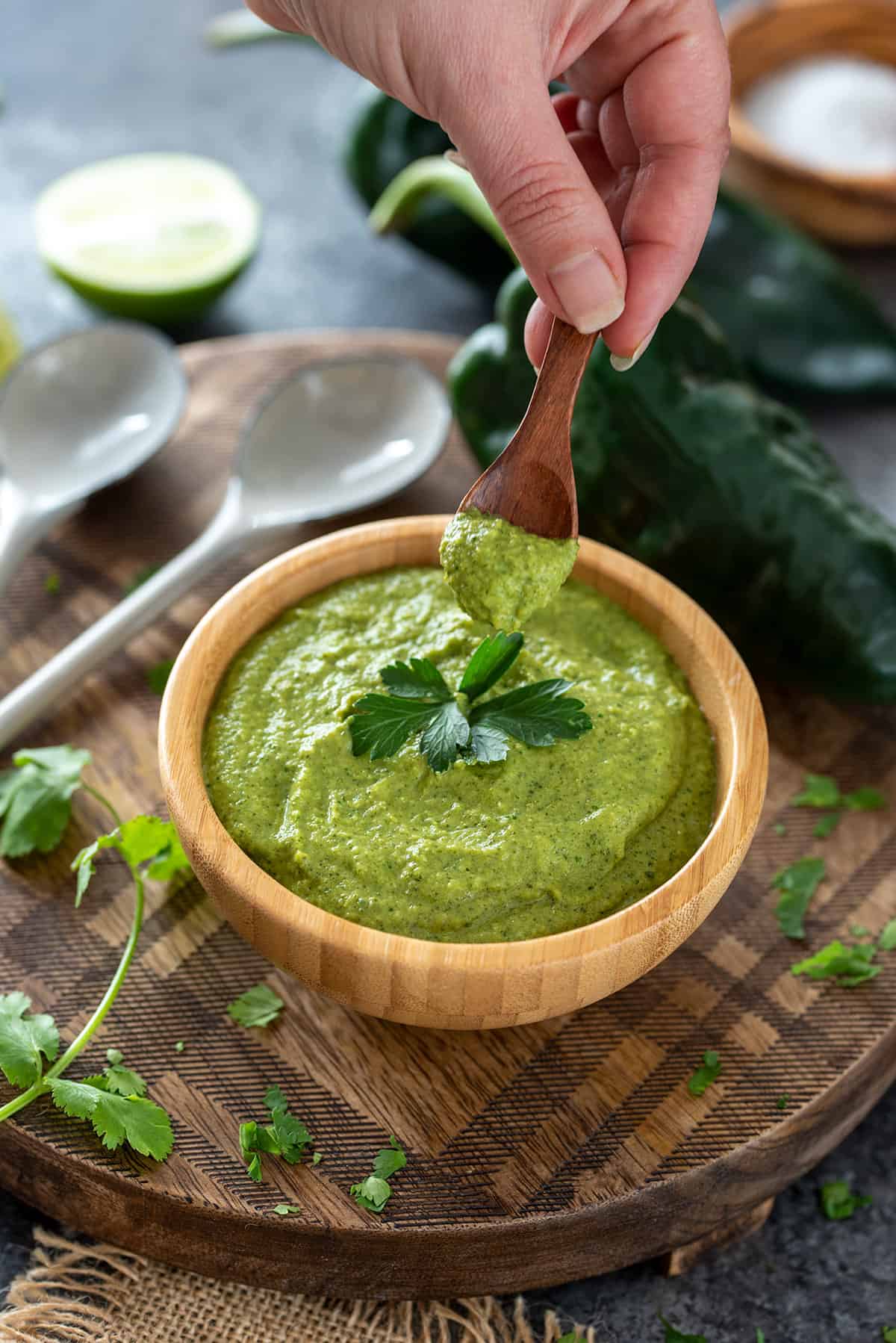 Woman picking up a spoon of poblano cream sauce in a bowl.
