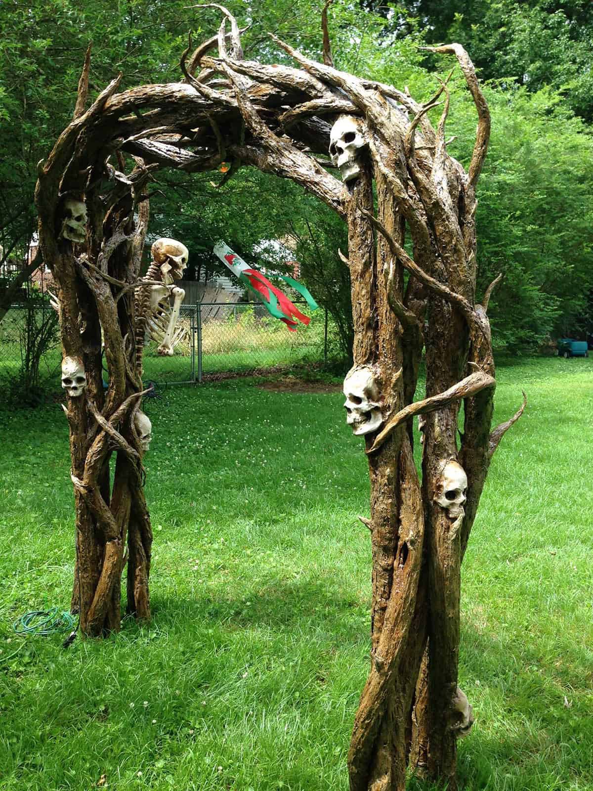 DIY Halloween archway features spooky skeletons nestled in tangled roots and vines over a PVC framework.