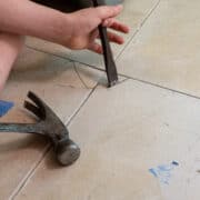 Hand holding a chisel to remove a broken tile.
