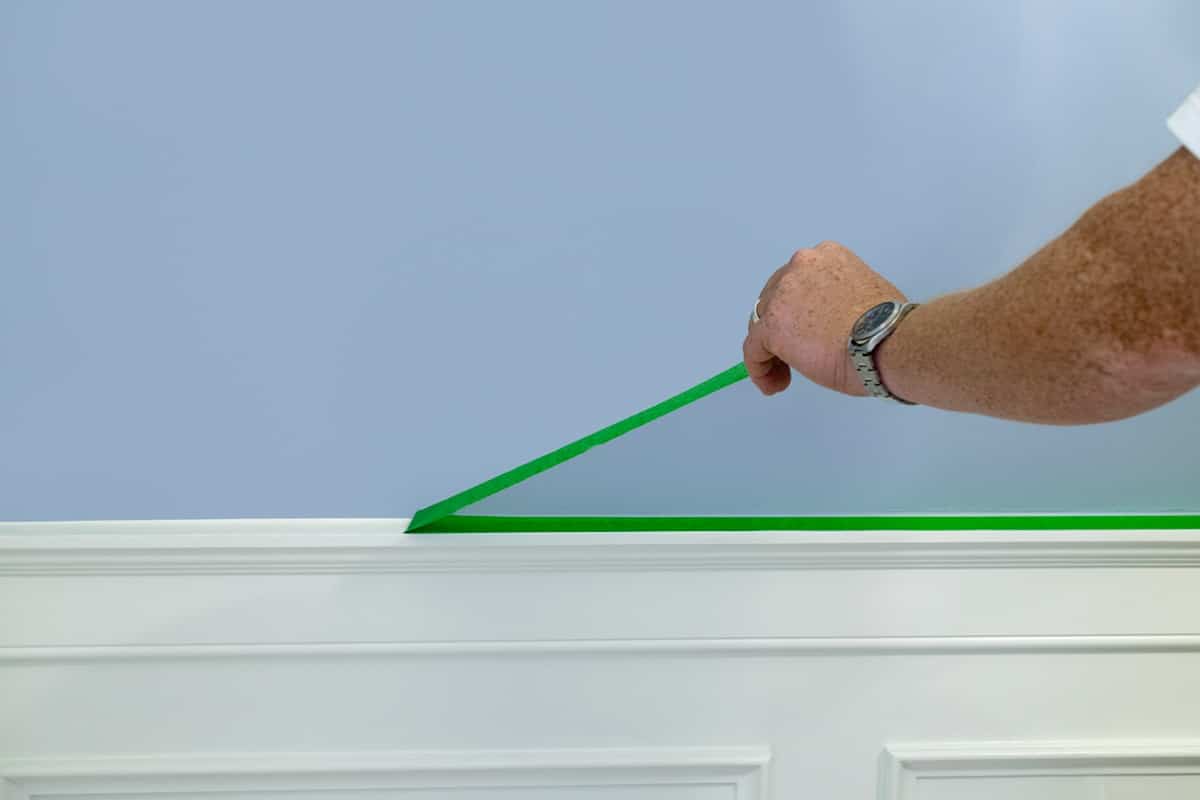 Frog tape being removed from top of wainscoting after painting main wall blue.