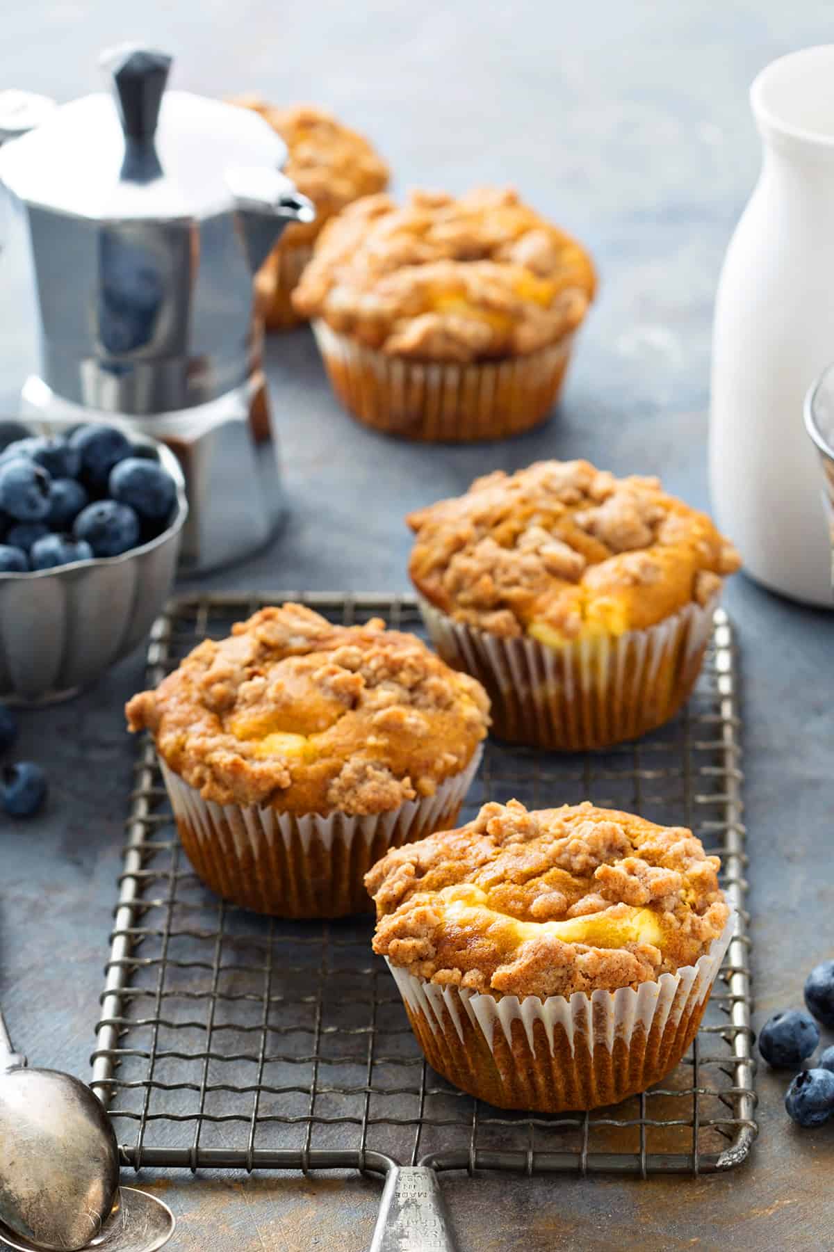 Three fall pumpkin cream cheese muffins with streusel topping on a wire cooling rack.