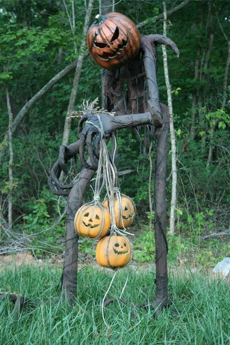 Giant Grim Reaper Pumpkin King figure with macabre face and willowy black body holding crude rope sack of jack-o-lanterns.