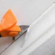 A caulk scraper removing the caulk on a baseboard.