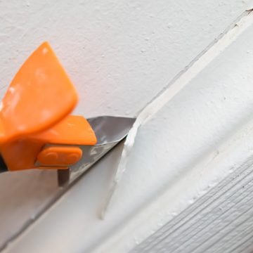 A caulk scraper removing the caulk on a baseboard.